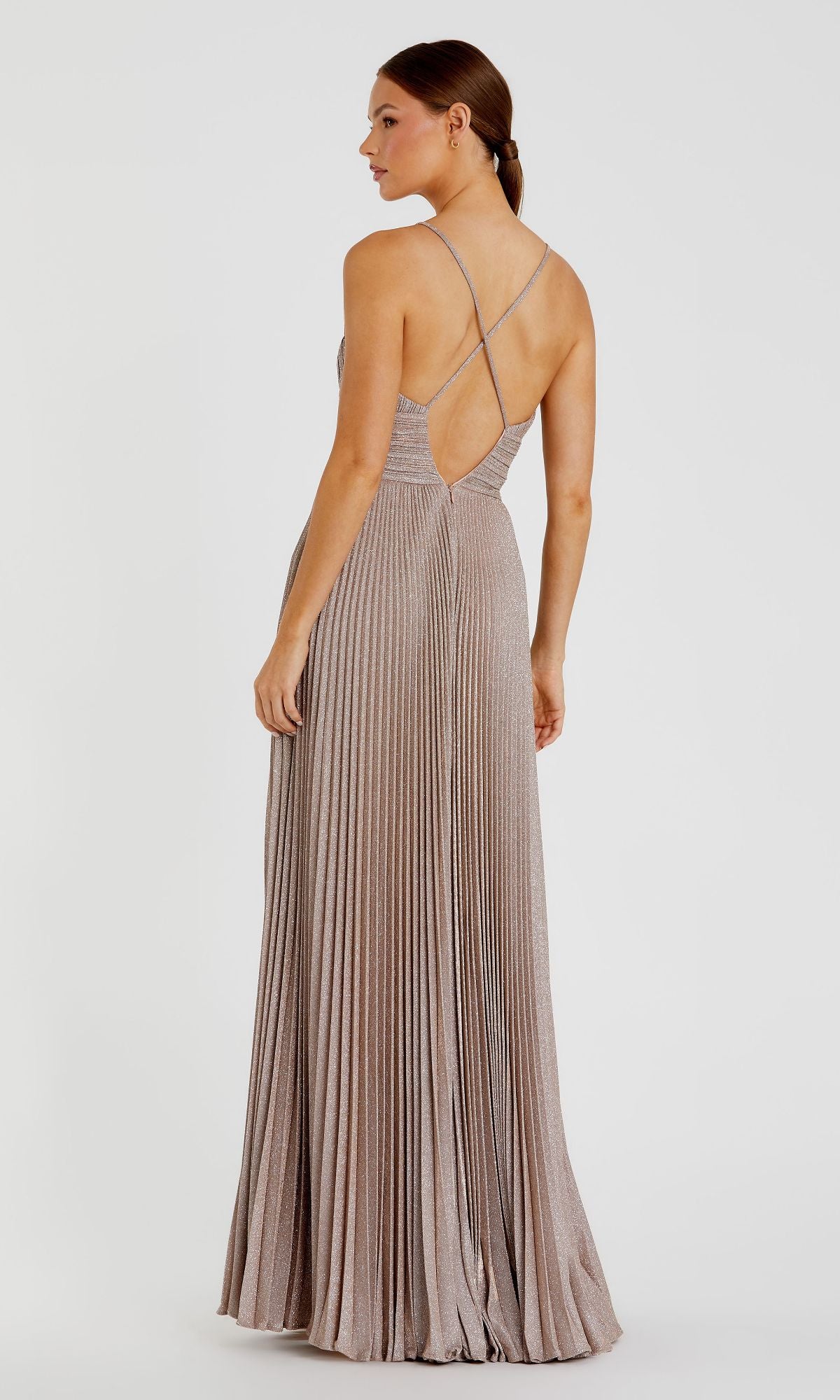 A woman stands facing away, wearing the Pleated Empire-Waist Long A-Line Prom Dress 30725, featuring metallic fabric, thin crisscross straps, an open back, and elegant pleats.